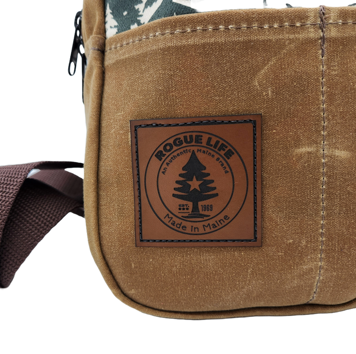 A close up image of the leather patch sewn to the front left pocket of the Stella bag. The original Rogue Lie Maine logo is laser etched, with the Rogue tree in the m,iddle, and the words Rogue Life on top. The bottom rocker says "Made in Maine."